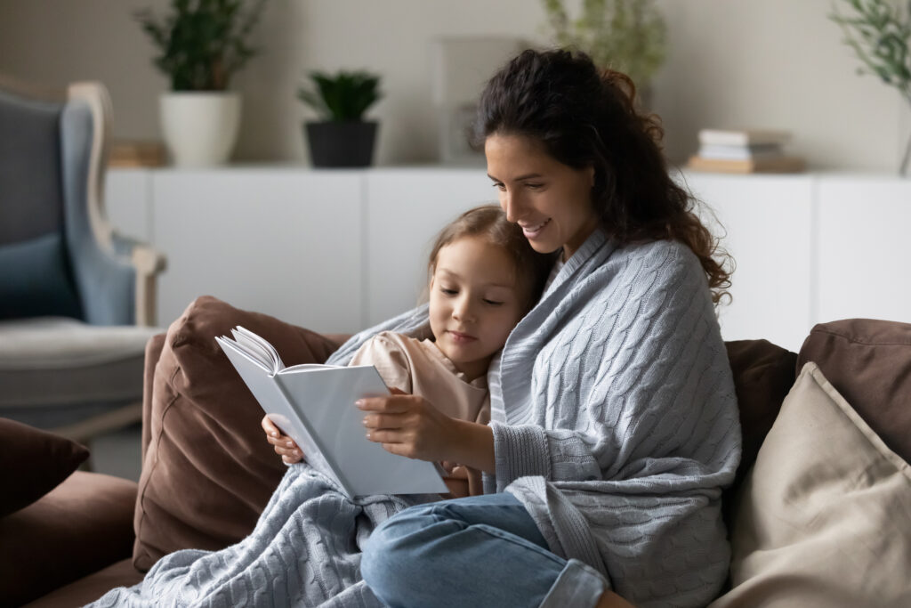 Mother and daughter staying warm reading on couch with blankets